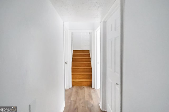 corridor with light wood-type flooring and a textured ceiling