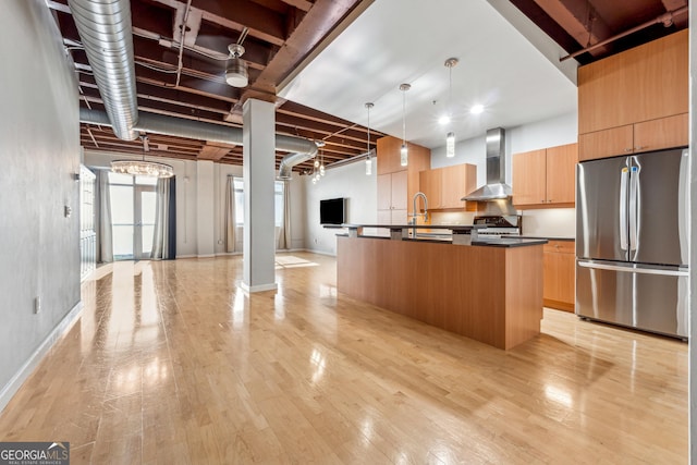 kitchen featuring light hardwood / wood-style floors, stainless steel fridge, a center island with sink, wall chimney range hood, and pendant lighting