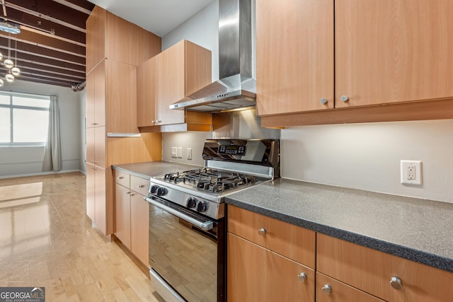 kitchen featuring beamed ceiling, stainless steel range with gas stovetop, light wood-type flooring, and wall chimney exhaust hood