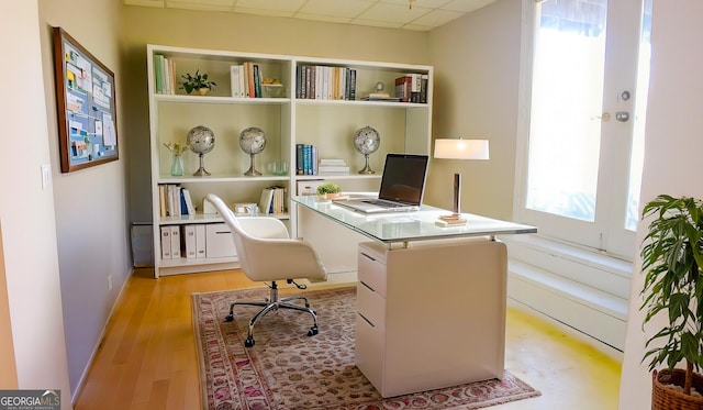 office area with a paneled ceiling, plenty of natural light, and light wood-type flooring