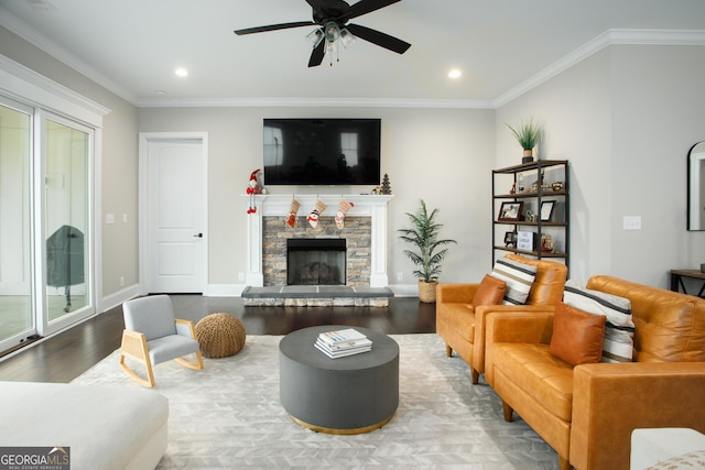 living room with hardwood / wood-style floors, a stone fireplace, ceiling fan, ornamental molding, and a healthy amount of sunlight