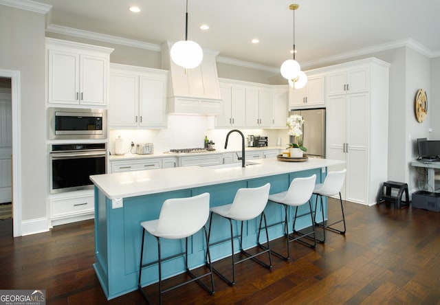 kitchen with a center island with sink, white cabinets, pendant lighting, and appliances with stainless steel finishes