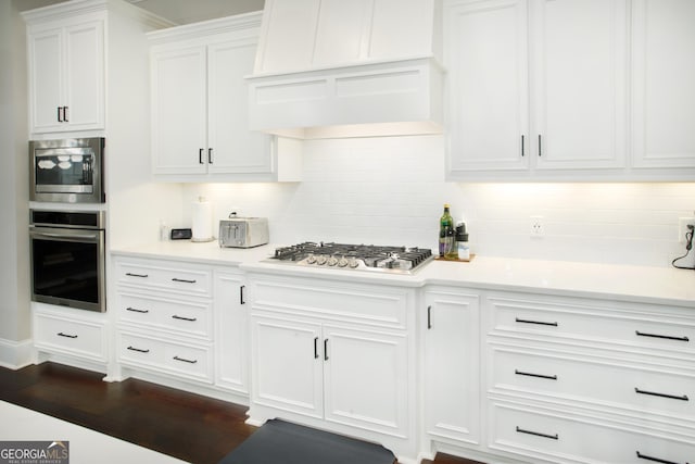 kitchen with dark hardwood / wood-style floors, backsplash, appliances with stainless steel finishes, white cabinets, and custom exhaust hood