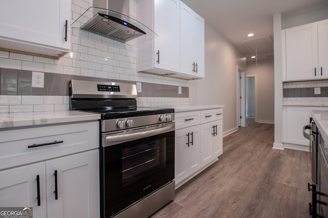 kitchen with light wood-type flooring, stainless steel stove, white cabinetry, and wall chimney exhaust hood