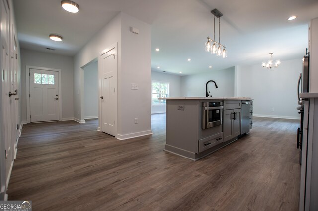 kitchen with stainless steel oven, a kitchen island with sink, dark hardwood / wood-style floors, gray cabinets, and hanging light fixtures