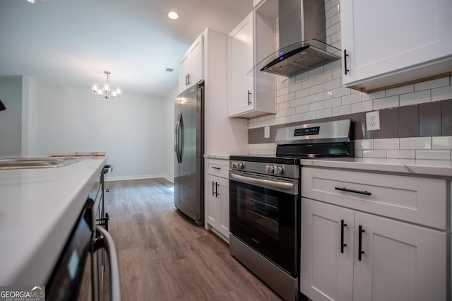 kitchen featuring stainless steel appliances, wall chimney range hood, an inviting chandelier, light hardwood / wood-style flooring, and white cabinets