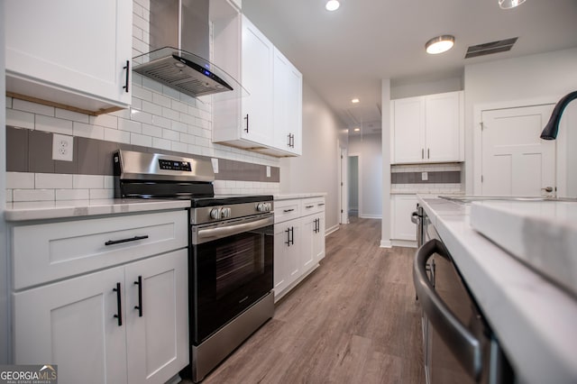 kitchen with white cabinetry, wall chimney exhaust hood, backsplash, light hardwood / wood-style floors, and appliances with stainless steel finishes