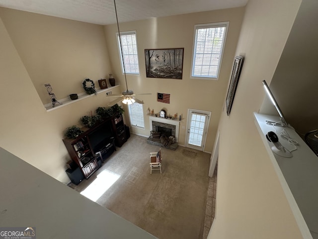 living room with ceiling fan, a stone fireplace, and carpet floors