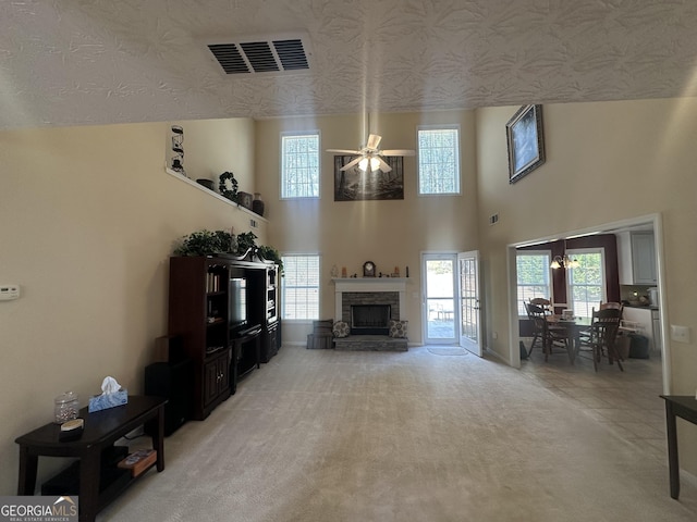 unfurnished living room with a stone fireplace, a ceiling fan, visible vents, and light colored carpet