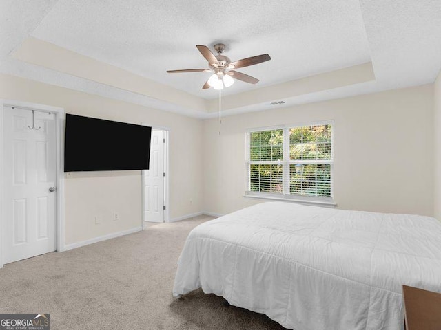 bedroom with ceiling fan, a raised ceiling, light colored carpet, and a textured ceiling