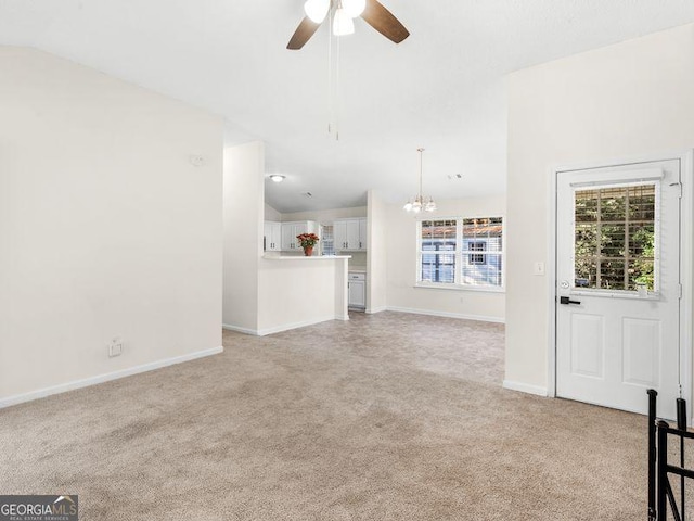 unfurnished living room featuring ceiling fan with notable chandelier, light colored carpet, and vaulted ceiling