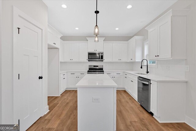 kitchen with a center island, sink, stainless steel appliances, pendant lighting, and white cabinets