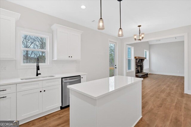 kitchen with white cabinetry, sink, hanging light fixtures, stainless steel dishwasher, and a fireplace