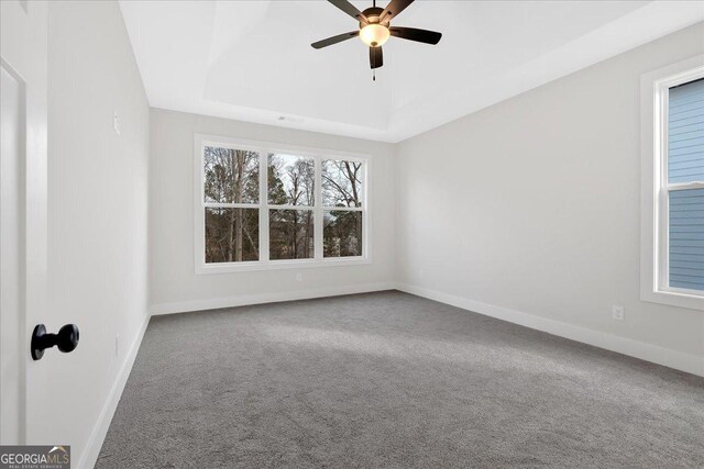 empty room with a tray ceiling, ceiling fan, and carpet floors