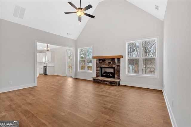 unfurnished living room featuring ceiling fan with notable chandelier, a healthy amount of sunlight, a fireplace, and high vaulted ceiling