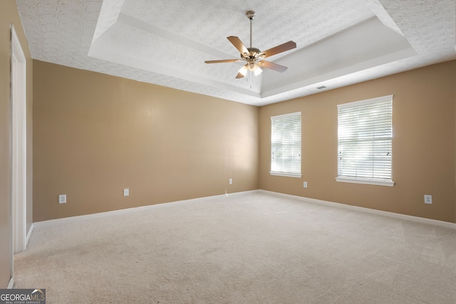 carpeted spare room with a tray ceiling, ceiling fan, and a textured ceiling