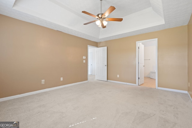 unfurnished bedroom featuring a textured ceiling, ensuite bathroom, a raised ceiling, and ceiling fan