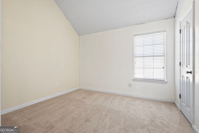 empty room with lofted ceiling, light carpet, and a textured ceiling