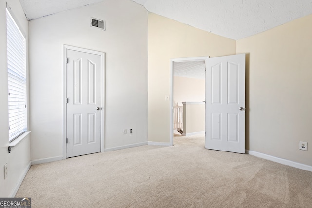 unfurnished bedroom featuring multiple windows, light colored carpet, a textured ceiling, and vaulted ceiling