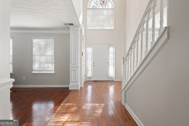 foyer featuring a textured ceiling, decorative columns, crown molding, and dark wood-type flooring