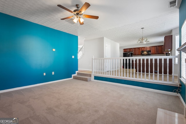 empty room featuring carpet, a textured ceiling, and ceiling fan with notable chandelier