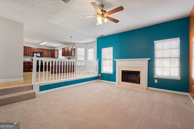 unfurnished living room with ceiling fan with notable chandelier, light colored carpet, a textured ceiling, and a wealth of natural light