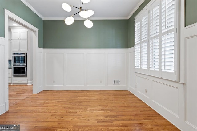 unfurnished dining area with crown molding, light wood-type flooring, and a notable chandelier