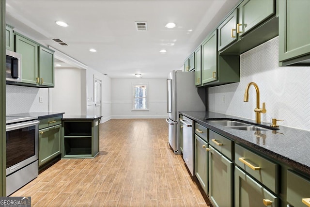 kitchen with appliances with stainless steel finishes, light wood-type flooring, dark stone counters, sink, and green cabinetry