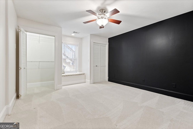 unfurnished bedroom with multiple closets, ceiling fan, and light carpet