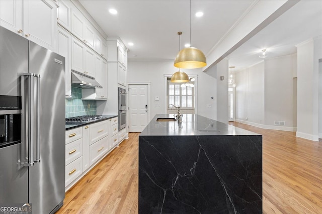 kitchen with decorative backsplash, an island with sink, decorative light fixtures, white cabinetry, and stainless steel appliances