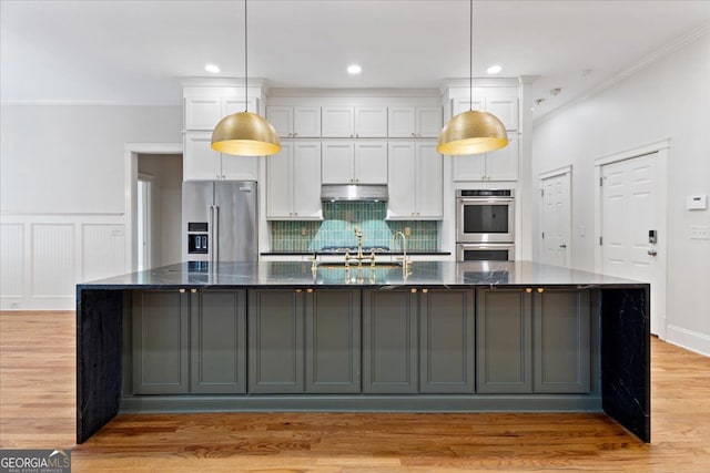 kitchen featuring white cabinetry, stainless steel appliances, a large island with sink, and dark stone counters