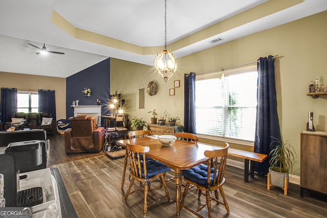 dining space with a raised ceiling, dark hardwood / wood-style flooring, and ceiling fan with notable chandelier