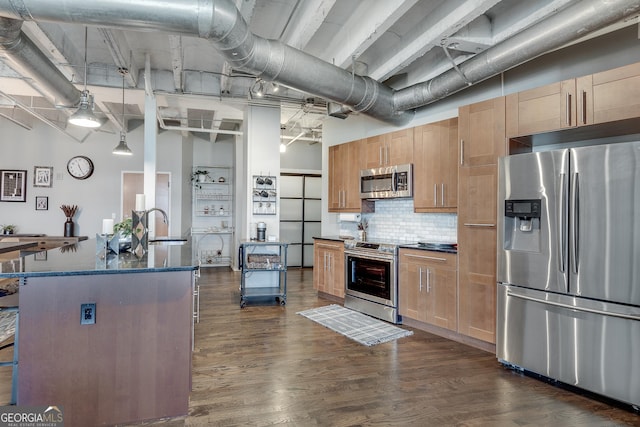 kitchen featuring sink, hanging light fixtures, a towering ceiling, an island with sink, and appliances with stainless steel finishes