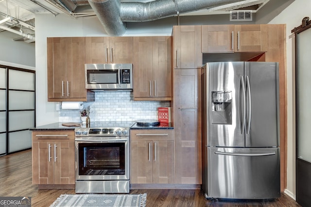 kitchen with stainless steel appliances, tasteful backsplash, a barn door, dark hardwood / wood-style floors, and dark stone counters