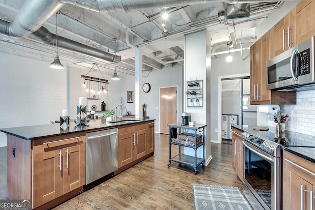 kitchen featuring sink, stainless steel appliances, a high ceiling, decorative light fixtures, and a center island with sink