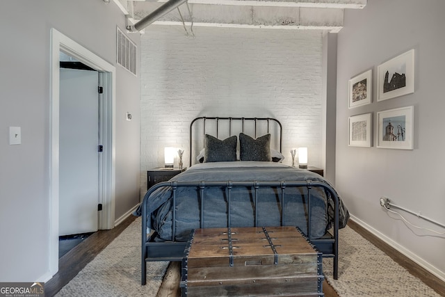 bedroom featuring dark hardwood / wood-style flooring, a towering ceiling, and brick wall