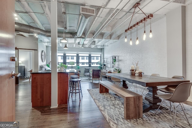 dining room featuring dark wood-type flooring, a towering ceiling, and brick wall