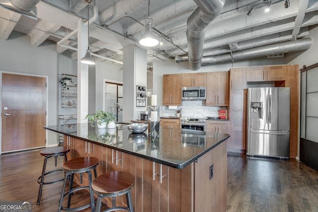 kitchen featuring a high ceiling, dark hardwood / wood-style flooring, dark stone counters, decorative backsplash, and appliances with stainless steel finishes