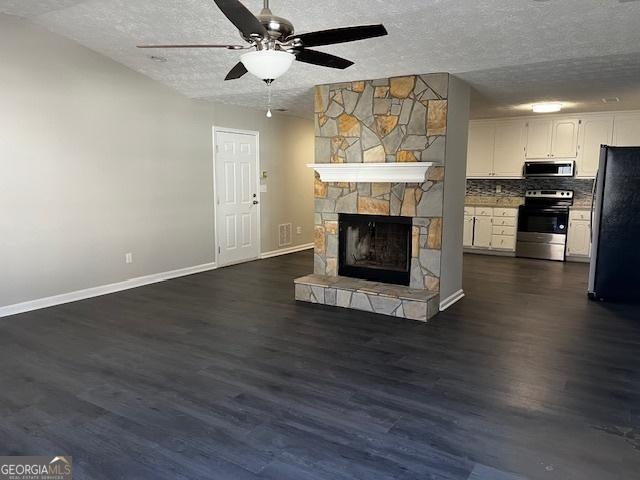 unfurnished living room with ceiling fan, a stone fireplace, a textured ceiling, and dark wood-type flooring