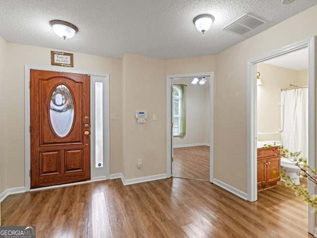 entryway with an inviting chandelier, a textured ceiling, and light hardwood / wood-style flooring