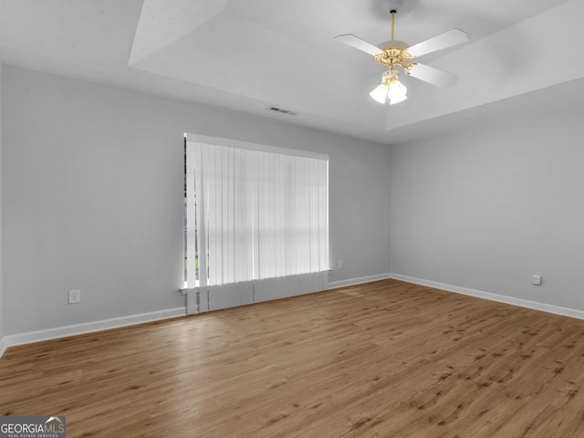 empty room featuring ceiling fan, a raised ceiling, and wood-type flooring