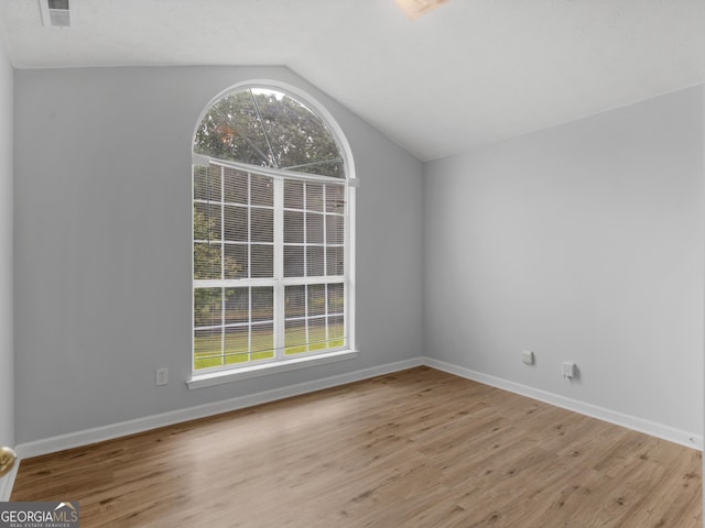 unfurnished room featuring a healthy amount of sunlight, lofted ceiling, and light hardwood / wood-style floors