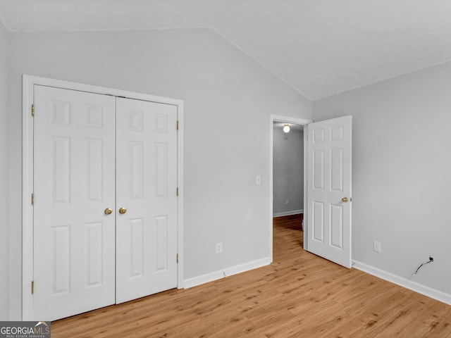 unfurnished bedroom with light hardwood / wood-style floors, lofted ceiling, and a closet