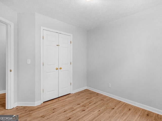 unfurnished bedroom with light wood-type flooring, a textured ceiling, and a closet