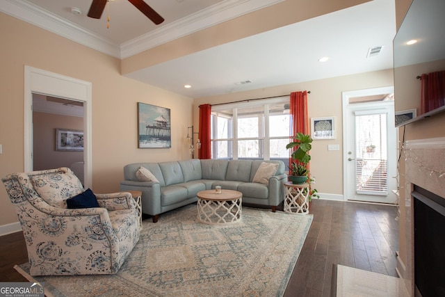 living area with visible vents, crown molding, baseboards, dark wood-type flooring, and a fireplace with flush hearth