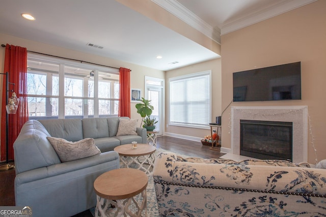 living area featuring wood finished floors, baseboards, visible vents, a fireplace, and crown molding