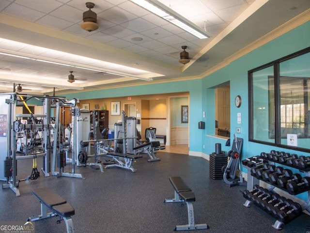 exercise room featuring a tray ceiling, a drop ceiling, crown molding, baseboards, and ceiling fan