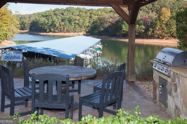 view of patio / terrace featuring a wooded view, an outdoor kitchen, a boat dock, a water view, and a grill