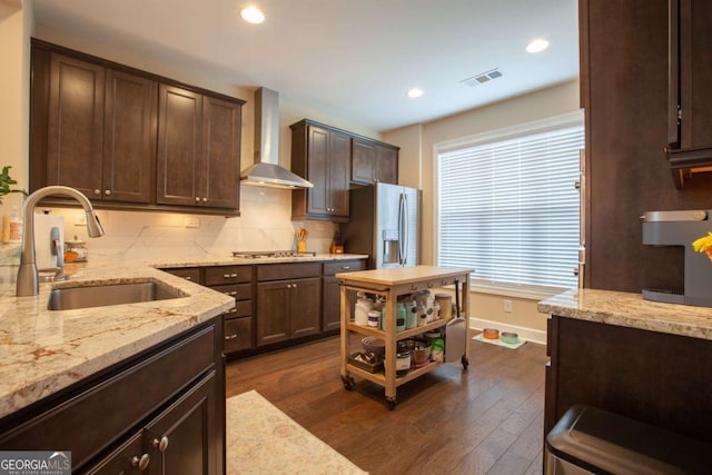 kitchen featuring dark wood-style floors, visible vents, a sink, stainless steel appliances, and wall chimney range hood