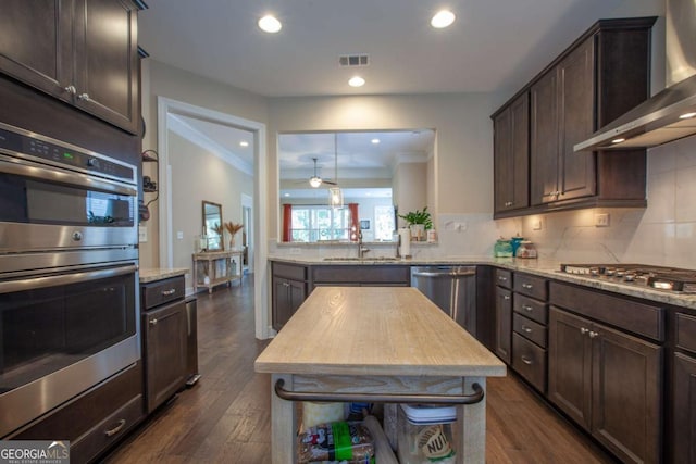 kitchen with visible vents, stainless steel appliances, wall chimney exhaust hood, decorative backsplash, and dark brown cabinets